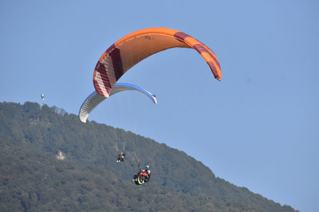 Two paragliders enjoying a thrilling flight in the clear blue sky, with a picturesque landscape beneath them.